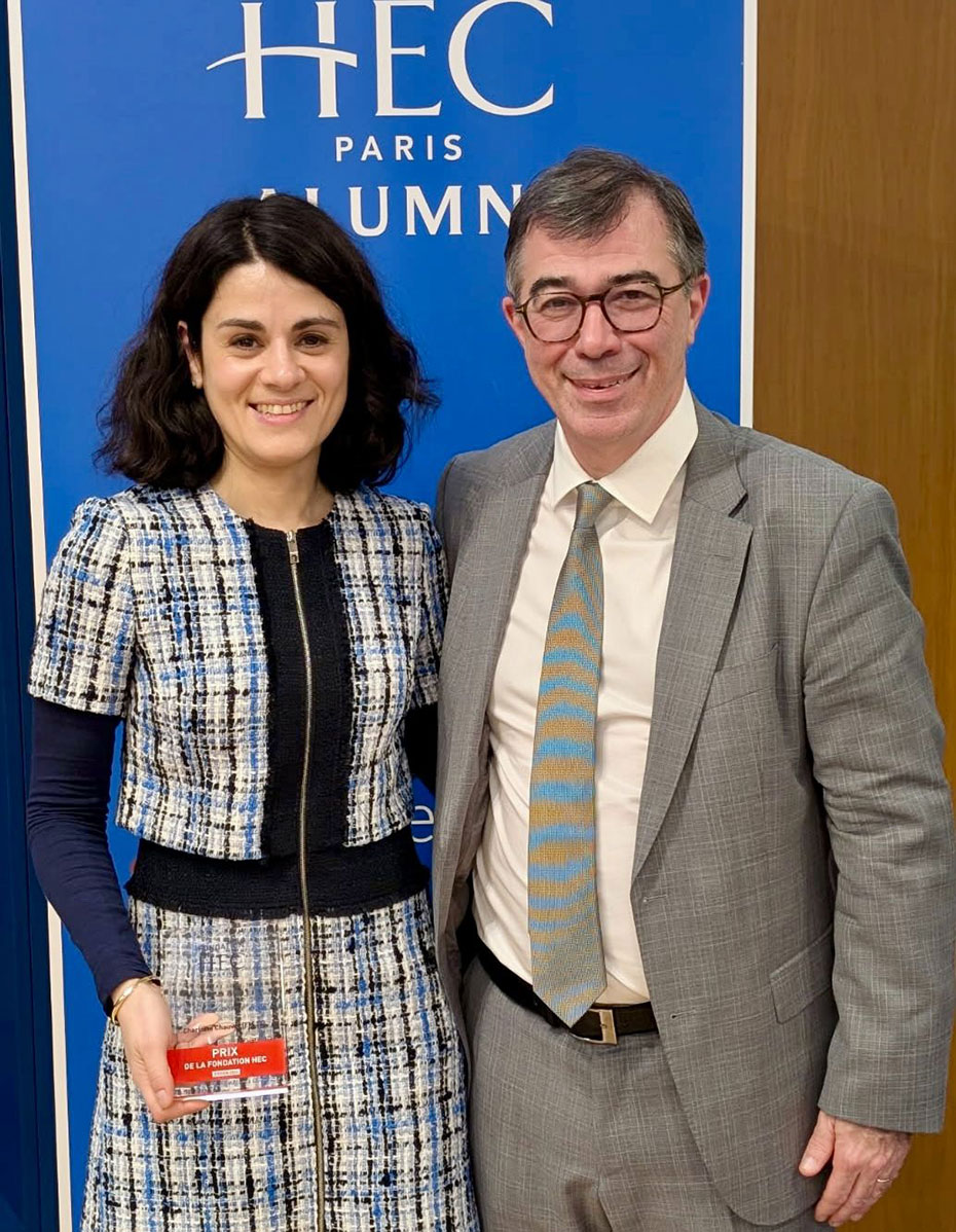 Charlotte Chauvel, souriante, tenant son prix de la Fondation HEC, aux côtés d'Olivier Stephan, devant un fond aux couleurs de HEC Paris Alumni.