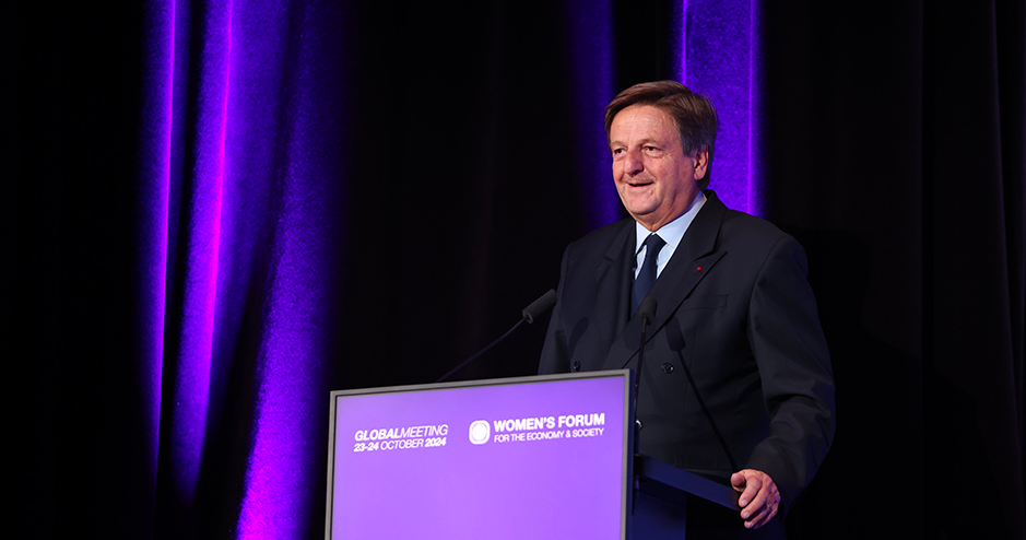 Jean-Luc Allavena, dressed in a dark suit, speaks at the Women’s Forum for the Economy & Society. He stands behind a purple podium displaying the event details: 'Global Meeting, 23-24 October 2024' and the Women’s Forum logo