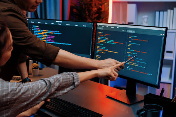 People discussing code displayed across two monitors in a room with neon lighting at a modern office.